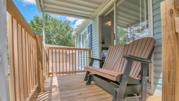 Una terraza de madera con una sola silla Adirondack y barandilla de madera.