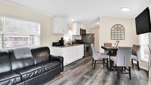 Un espacio habitable compacto con kitchenette, zona de comedor y sala de estar con sofá y sillas.
