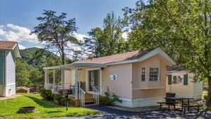Una casa móvil de un piso con un porche, una estructura pequeña adosada y una mesa de picnic.