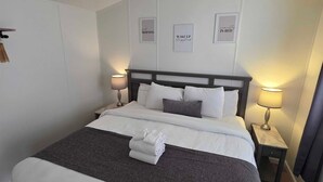 Un letto rifatto con copriletto grigio e bianco, due comodini con lampade e tre poster motivazionali incorniciati appesi al muro.