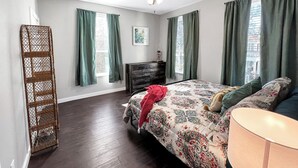Une chambre à coucher avec un lit, une commode, un ventilateur de plafond et une fenêtre avec des rideaux.