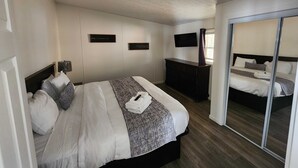 Habitación de hotel con cama, cómoda, televisor montado en la pared y armario con puerta corredera.