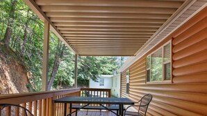 Una terraza cubierta al aire libre con mesa y sillas, rodeada de paredes de madera y vistas a árboles.
