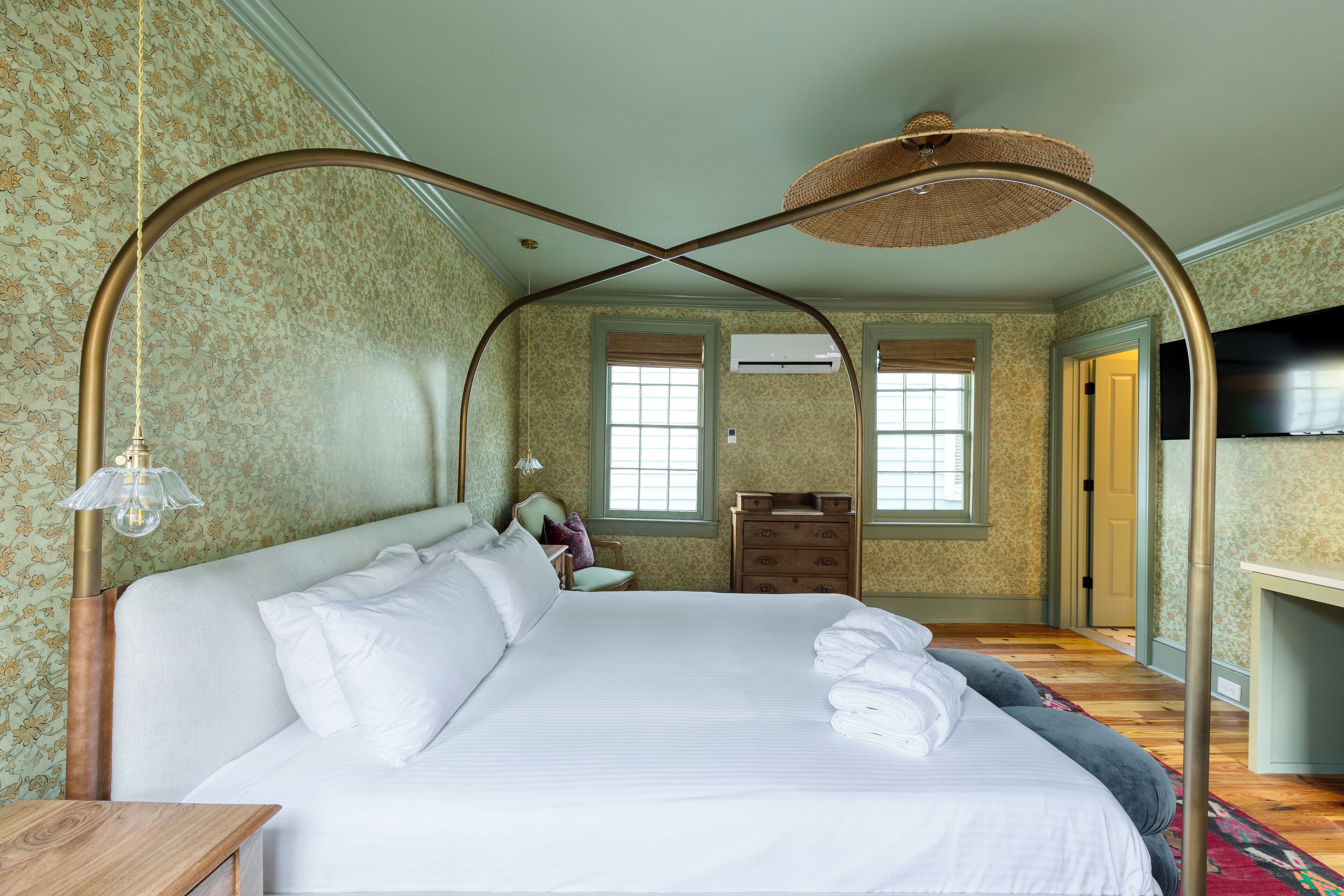 Un dormitorio ordenado con una cama con dosel, un aparador de madera y un televisor sobre un mueble.
