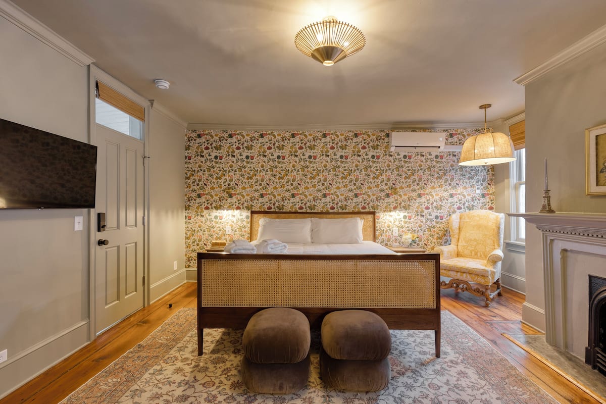 A bedroom with a large bed, a chair, a fireplace, and a television.