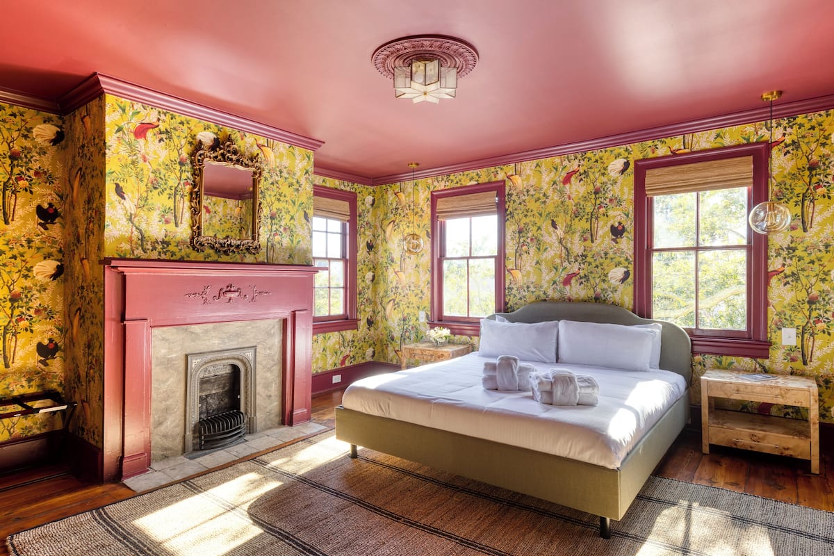 A room with a large bed, a fireplace, and floral wallpaper.