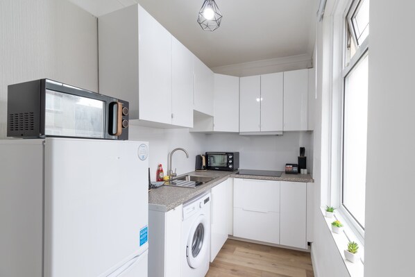 Compact kitchen with washing machine, microwave, sink, and toaster.