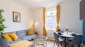 A modern living room with a sofa, a glass coffee table, and a dining area with chairs and a table set for two.
