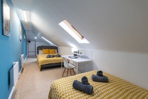Cozy retreat with two beds, a desk, and a seating area, featuring a skylight and framed artworks.