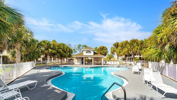 A swimming pool with lounge chairs, surrounded by palm trees and a building in the background. - Hidden Palms! Next to Shipwreck Island! (Panama City Beach)