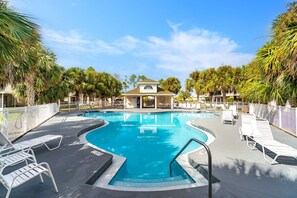A swimming pool with lounge chairs, surrounded by palm trees and a building in the background.