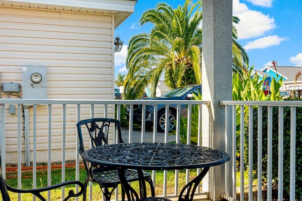 A balcony with a metal table and chairs, a white railing, and a palm tree in the background.