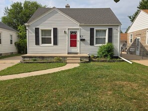 A single-story house with a red door, white siding, and a small front yard.