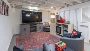Un salon équipé d’un téléviseur à écran plat, d’un canapé gris, d’un tapis rouge et d’une console de jeux.