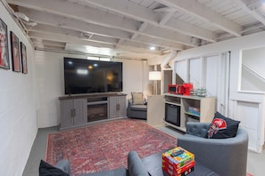 A living room with a flat-screen TV, grey sofa, red rug, and a game console.