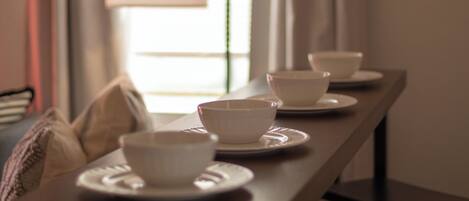 A dining table with white bowls and plates, a lamp, and a window with curtains.