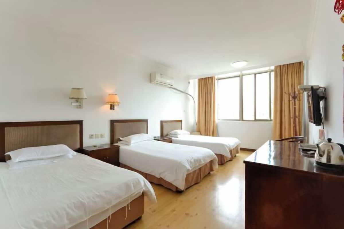 Hotelkamer met twee bedden, een bureau, een stoel, een lamp, een airconditioning en een raam met gordijnen.