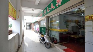 Un pasillo con un patinete aparcado a la izquierda, una tienda con un letrero verde a la derecha y una puerta visible.