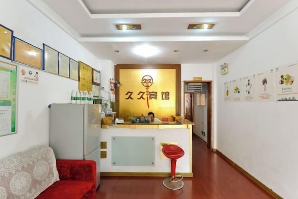 A reception area with a desk, a red chair, a sofa, and framed certificates on the wall. - Taizhou Jiujiu Hotel (Taizhou)