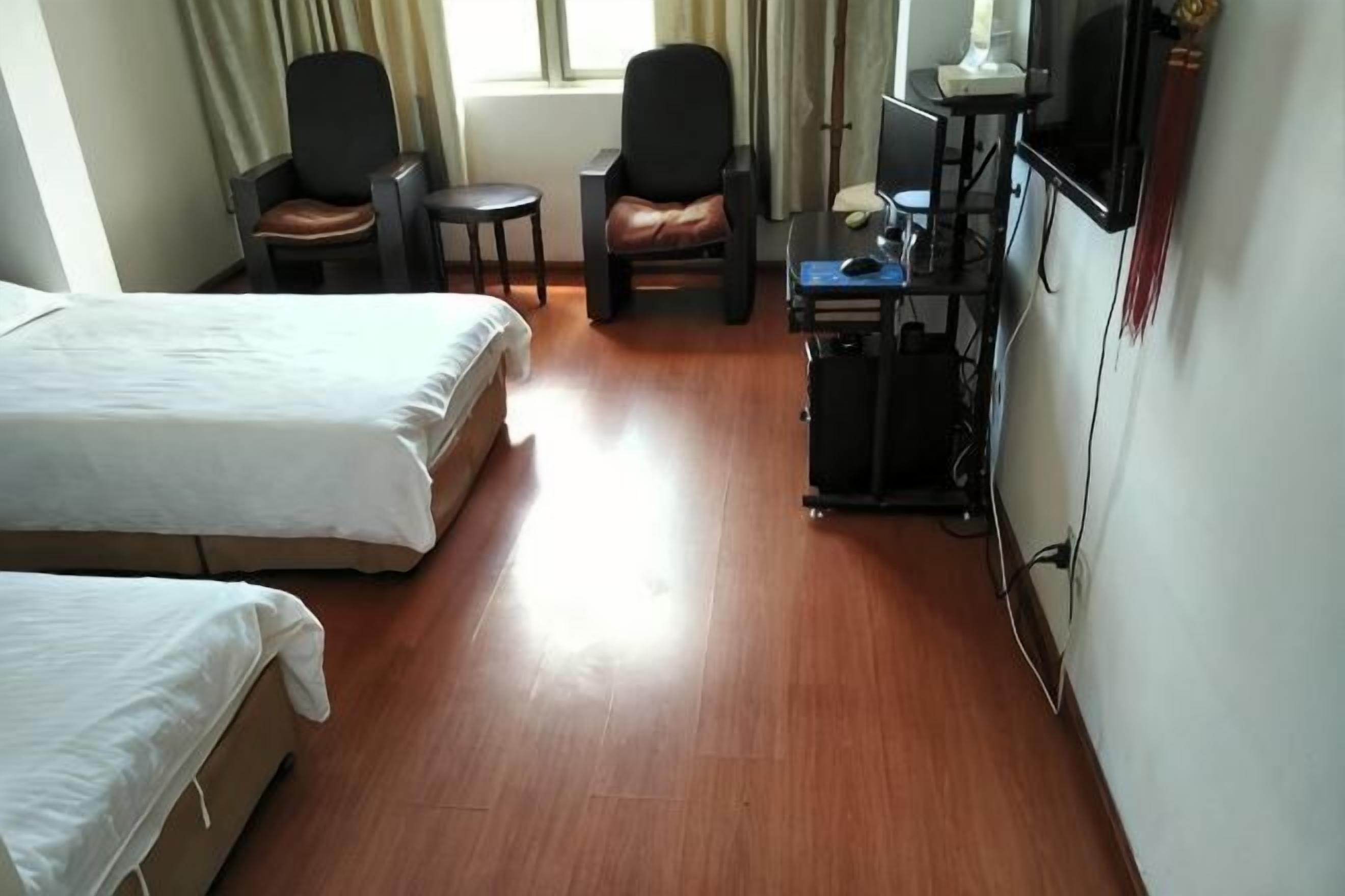 Ein Hotelzimmer mit zwei Betten, einem Schreibtisch, einem Stuhl, einem kleinen Tisch und einem Fernseher.