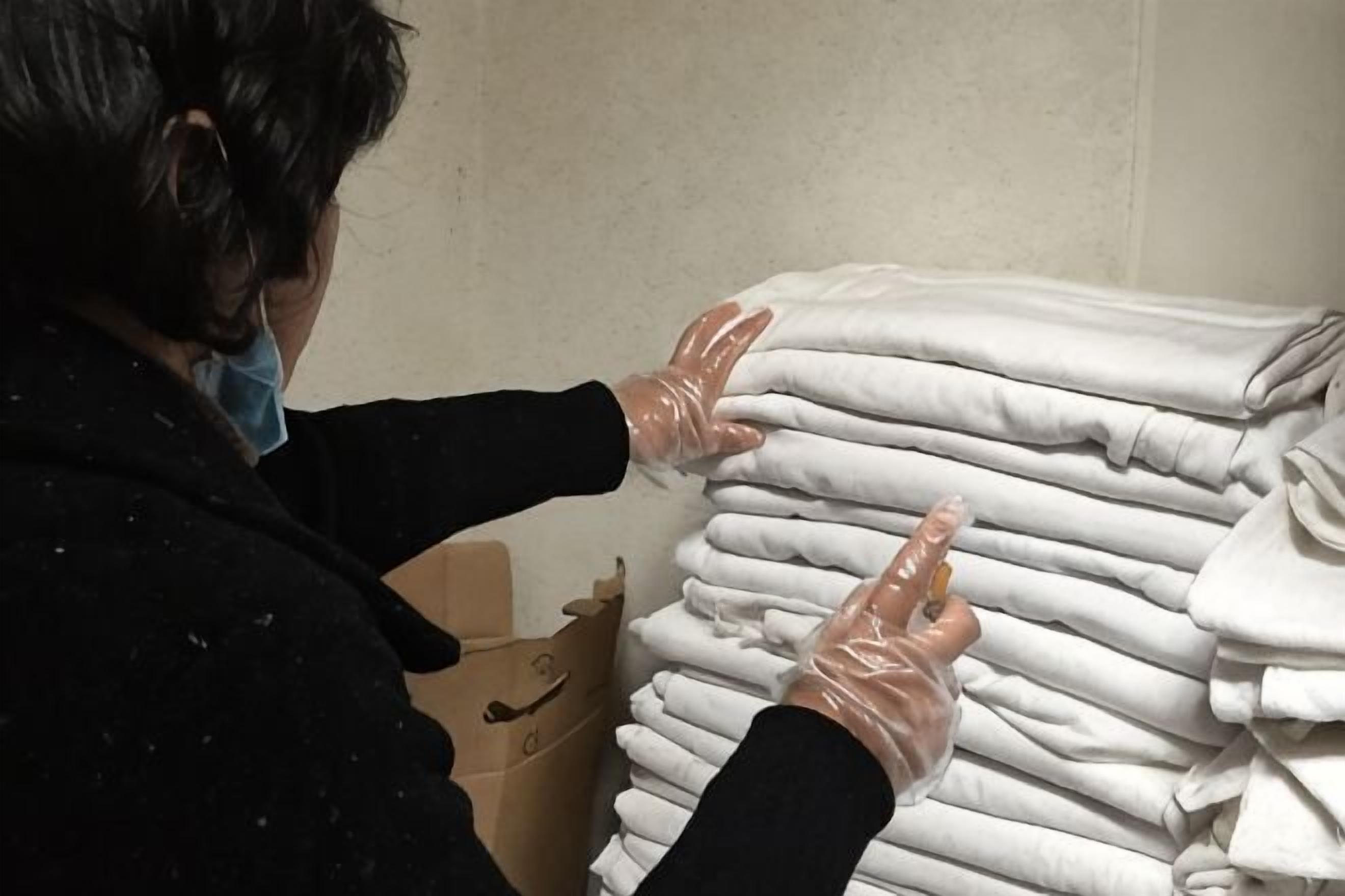 A person handling folded white towels, a cardboard box, and a plastic bag.