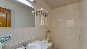 Un baño con lavamanos de mármol, estante de vidrio, inodoro y zona de ducha.