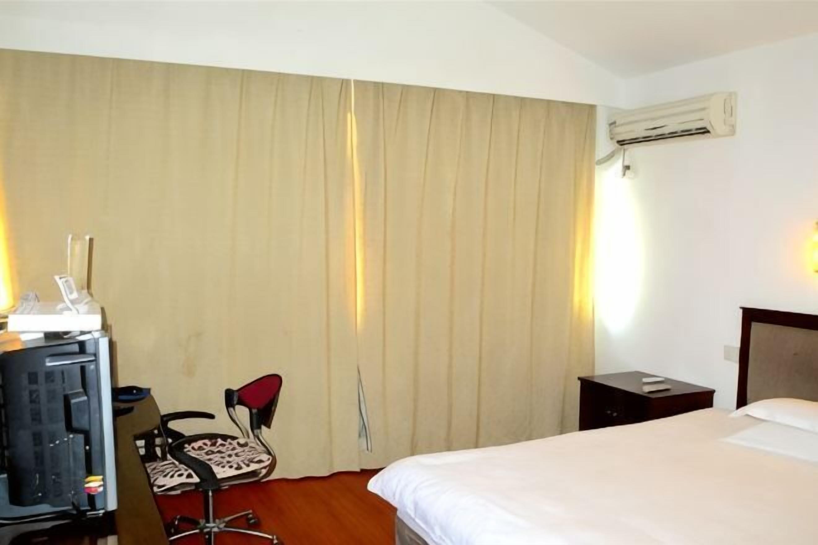 Ein Hotelzimmer mit einem Bett, einem Schreibtisch mit Computer, einem Sessel, einem Nachttisch und einer Klimaanlage.