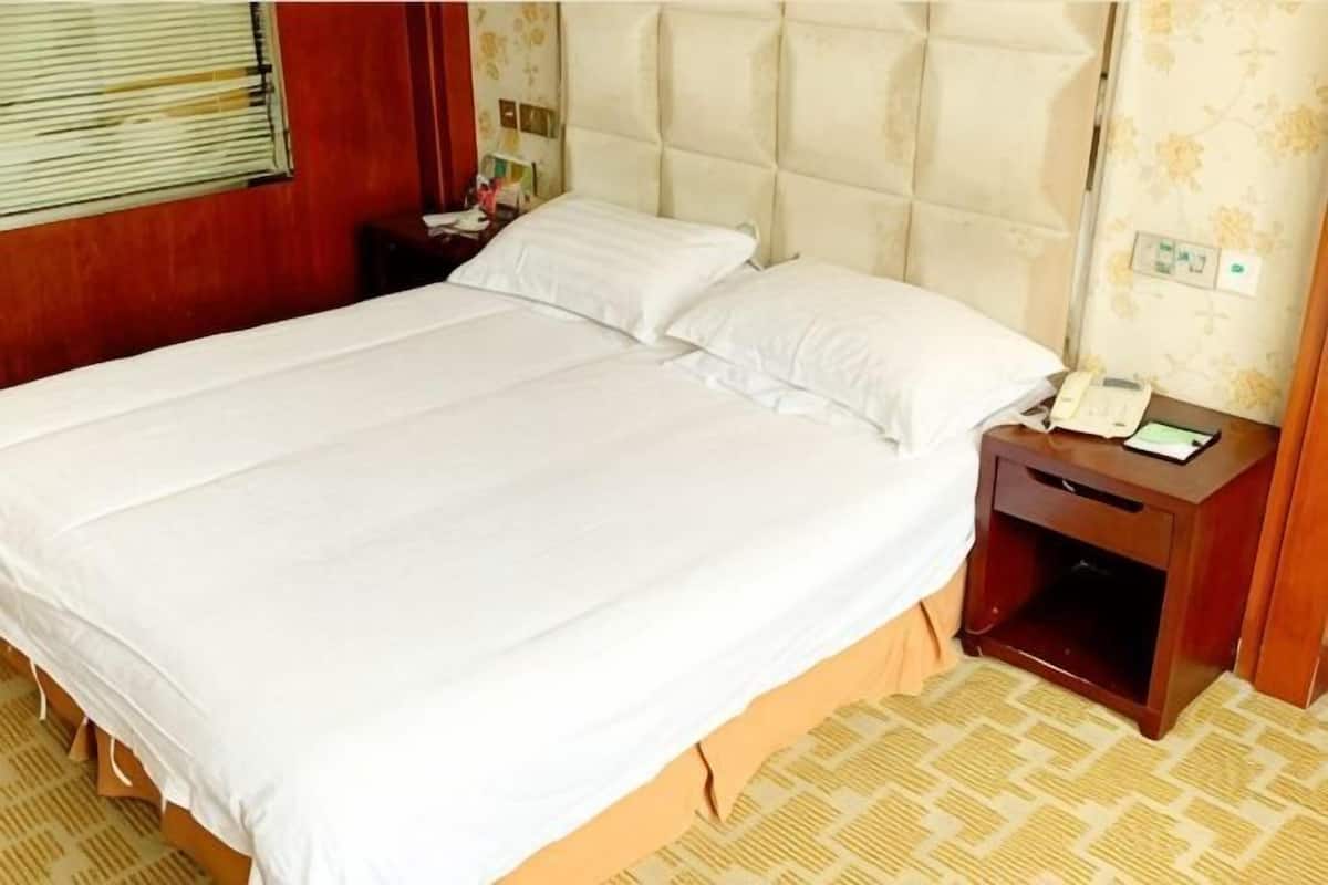 Een hotelkamer met een groot bed, een houten nachtkastje met een telefoon en een kamerbreed tapijt.