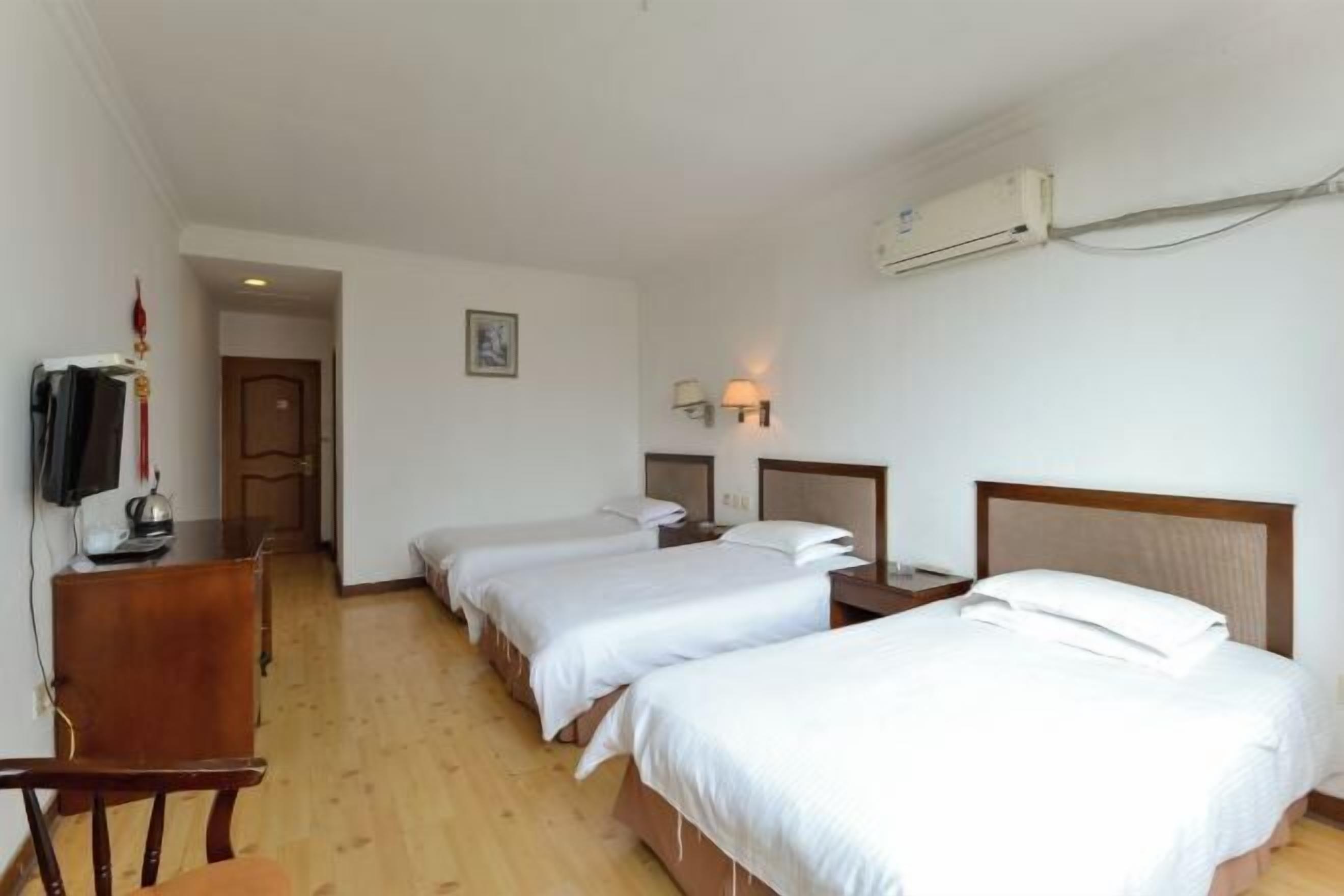A hotel room with two single beds, a desk with a chair, a TV, and an air conditioning unit.