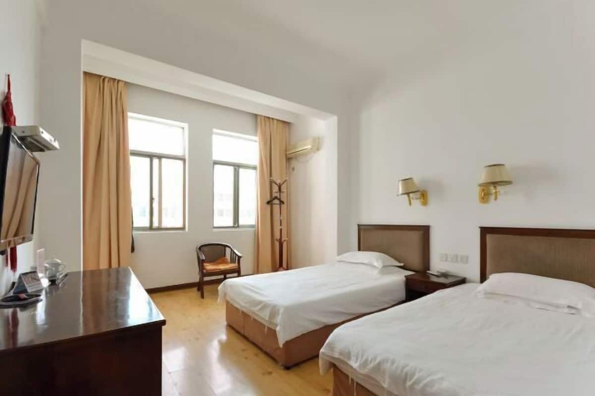 Een hotelkamer met twee bedden, een bureau, een stoel en een raam met gordijnen.