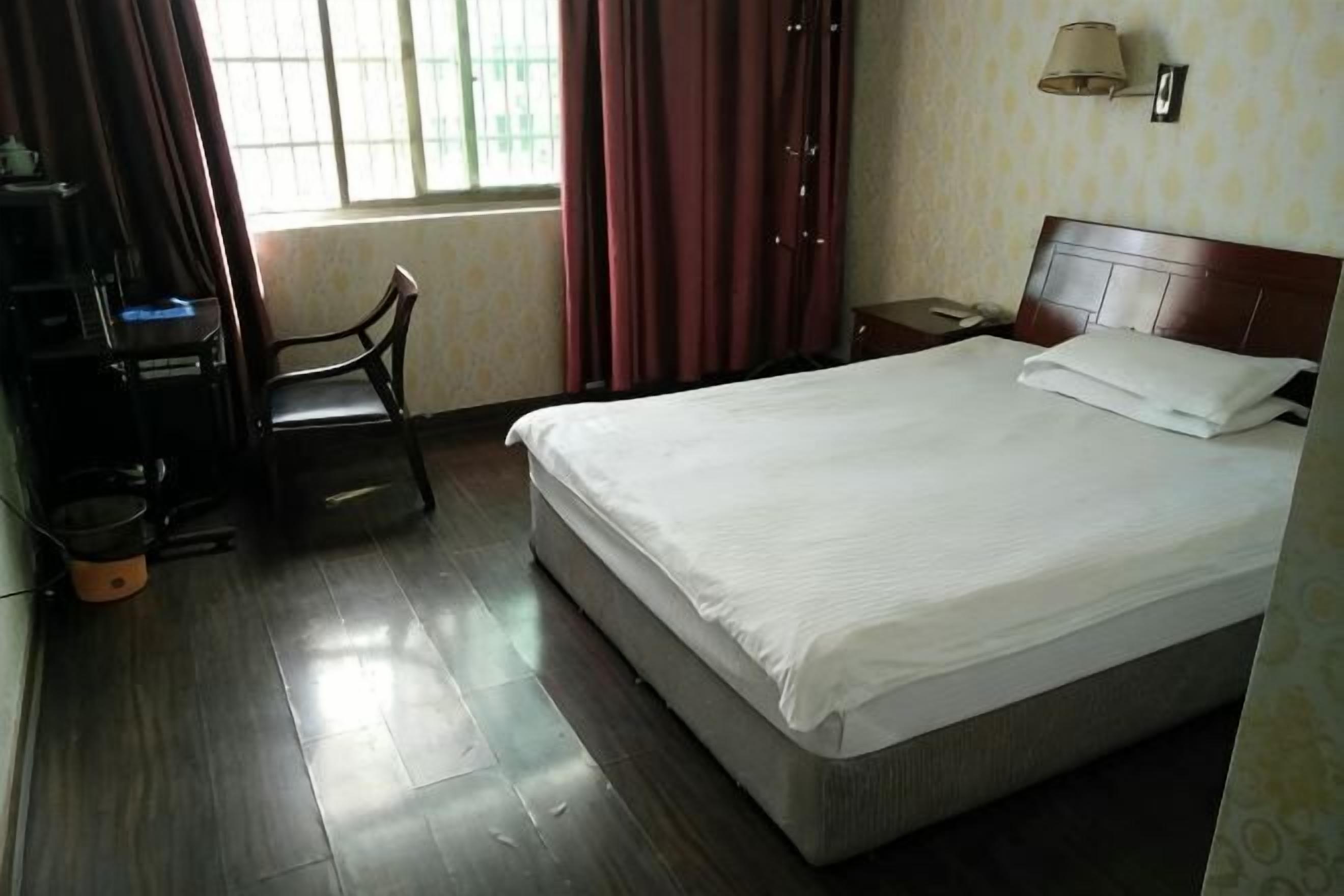 Una camera d'albergo con un letto, una scrivania, una sedia, un comodino e una finestra con tende.
