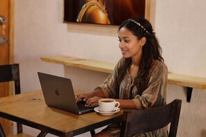 Uma pessoa sentada à mesa de madeira com um laptop e uma chávena de café.