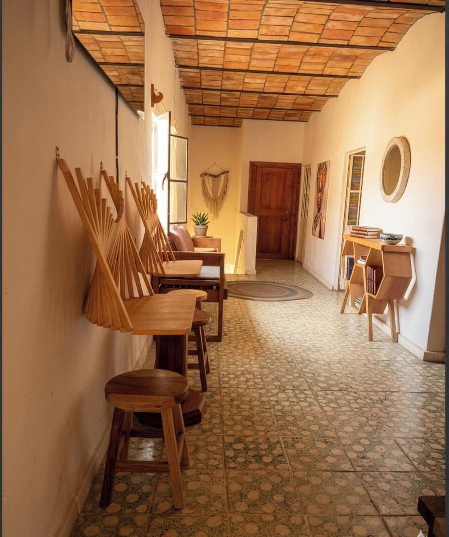 A hallway with wooden chairs and tables, a tiled floor, and a wooden door at the end.