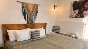 Una cama con cabecera de madera, colcha a rayas verdes y un macramé colgado en la pared.