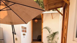 Un espacio al aire libre cubierto con un banco de madera, una mesa con libros, una planta en maceta y una escalera que conduce a una habitación interior.