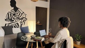 Una persona trabajando en un ordenador portátil sobre una mesa de cristal en una habitación moderna con un cuadro mural geométrico, un sofá y una planta pequeña.