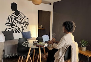A person working on a laptop at a glass table in a modern room with a geometric wall art, a sofa, and a small plant.