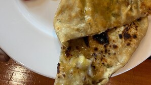 Egy tányér, rajta egy darab lapos kenyér, egy tál leves és egy kis tálka mártás.