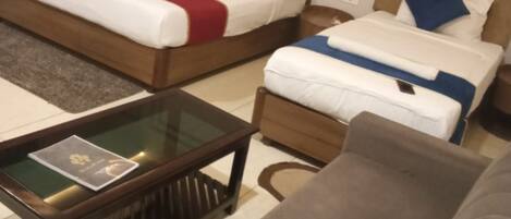 A hotel room with two beds, a sofa, and a glass-top coffee table.