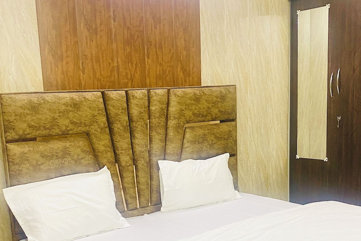 Una cama bien tendida con sábanas blancas en una habitación con paneles de madera y un espejo grande.