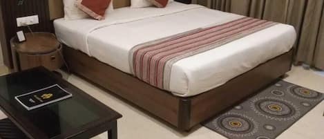 A hotel room with a bed, a bedside table, a small round table, and a patterned rug.