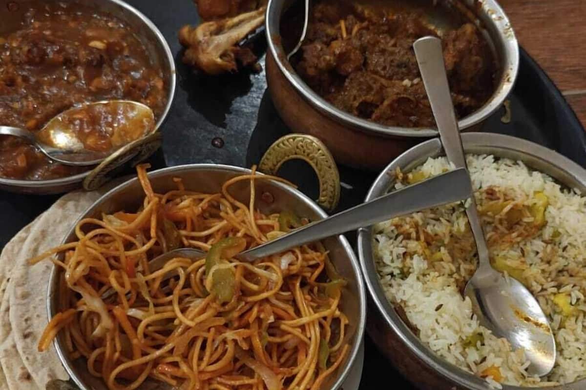Una bandeja negra con diversos platos de la cocina india, incluyendo arroz, fideos y curry.