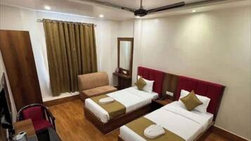 A hotel room with two single beds, a desk with a chair, a small table with a kettle, and a mirror on the wall.