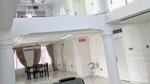 A spacious, multi-level interior with a high ceiling, chandeliers, and a balcony with glass railings. - 4BR Villa Pvt Pool, Rooftop. 10m walk to Beach. Starlink. Free Airport pick up  (Accra)