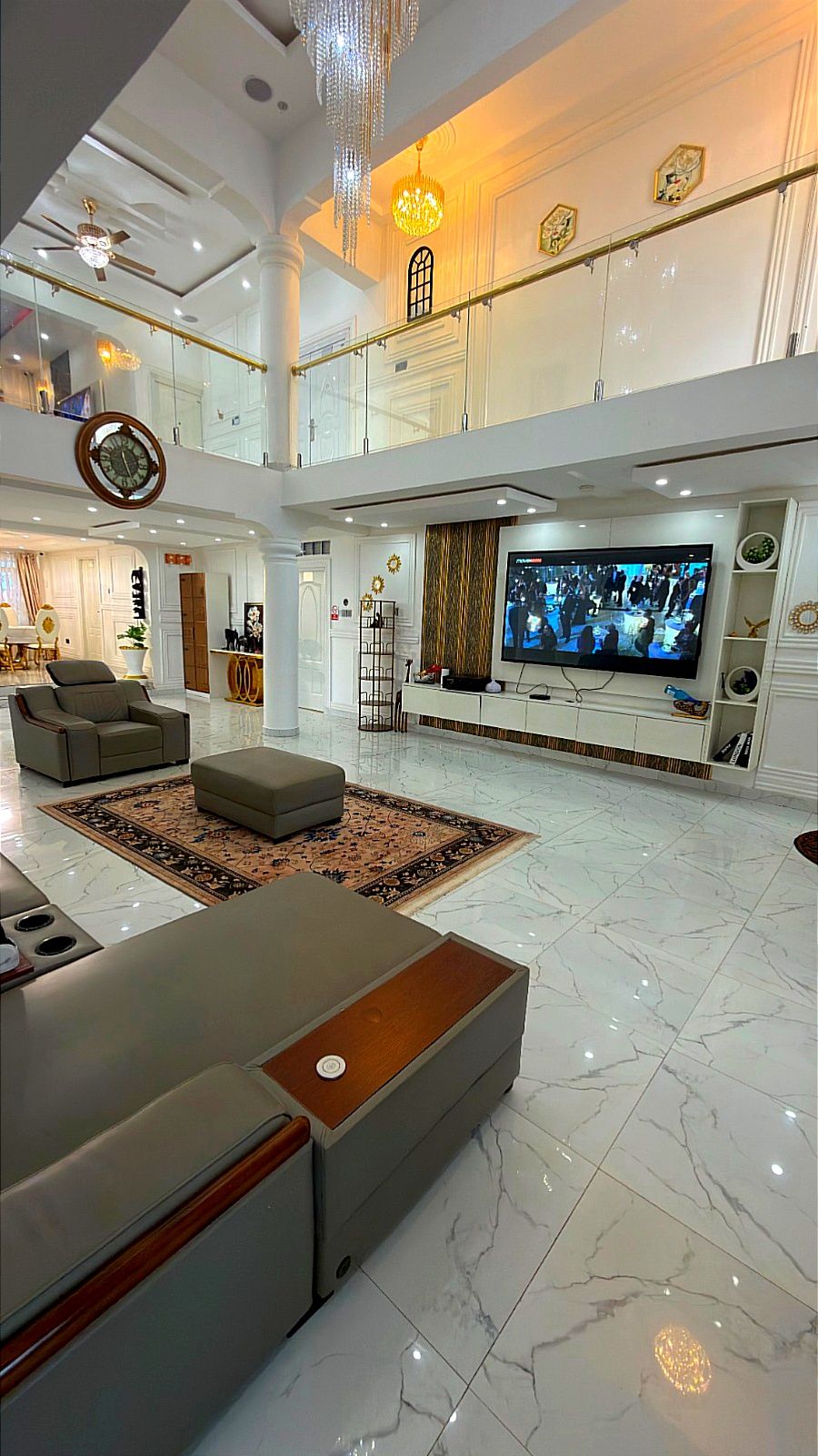 A spacious living area with a large flat-screen TV, a ceiling fan, and a chandelier.