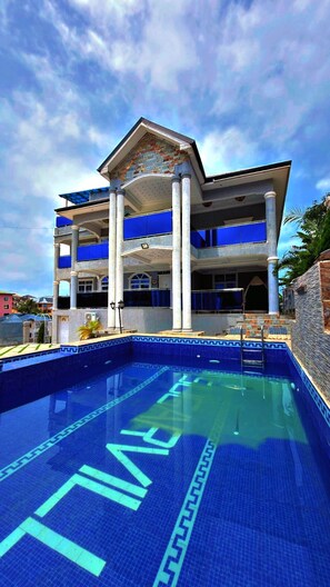 A hotel with a swimming pool, multiple balconies, and a clear sky.