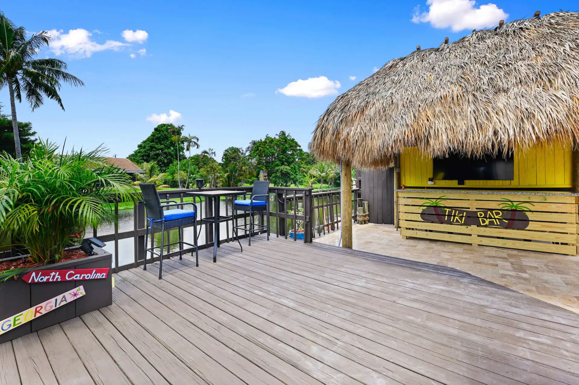 Eine Holzterrasse mit einer strohgedeckten Struktur, auf der die Aufschrift „TIKI BAR“ zu sehen ist, und einem Schild, das „North Carolina“ und „Georgia“ ausweist.