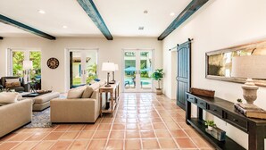 A spacious living area with a sofa set, a coffee table, and a TV on a stand. There is a door leading to a balcony with a view of greenery. - Sedona Style Resort home awaits your company! (Fort Myers)