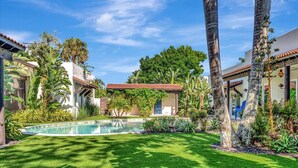 A well-maintained garden with a swimming pool, palm trees, and a small building with a tiled roof. - Sedona Style Resort home awaits your company! (Fort Myers)