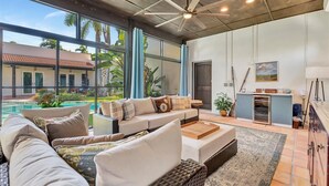 A spacious living area with a large sofa, a coffee table, and a view of a swimming pool and outdoor patio. - Sedona Style Resort home awaits your company! (Fort Myers)